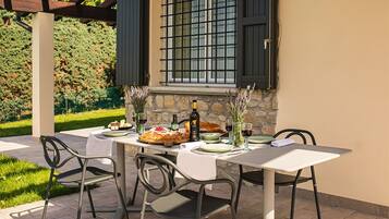 An outdoor dining area with a table set for two, surrounded by stone walls and a pergola.