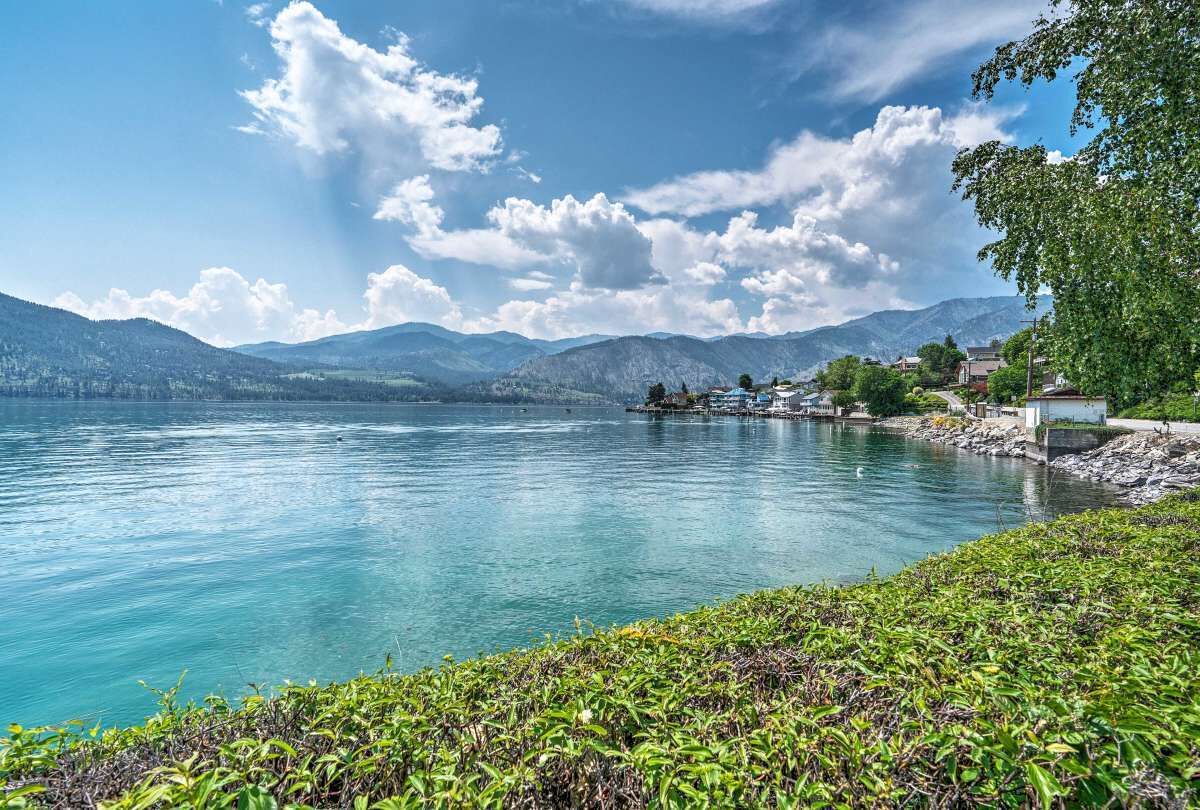 A lakeside view with mountains in the background, a dock, and a small building near the water.