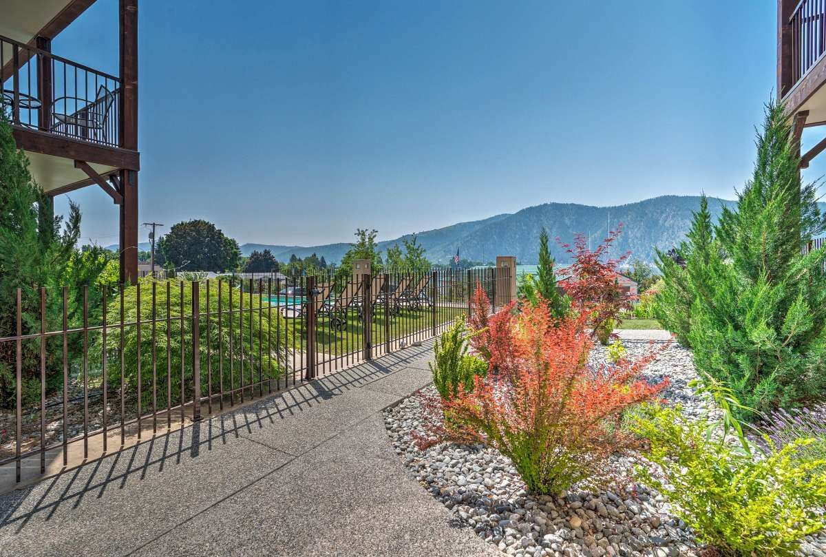 A pathway leading to a building with a metal fence, surrounded by greenery and a mountain in the background.