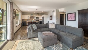 A spacious living area with a gray sectional sofa, a small ottoman, and a large rug. - Majestic Views / Lake Chelan / Pool and Spas! (Manson)