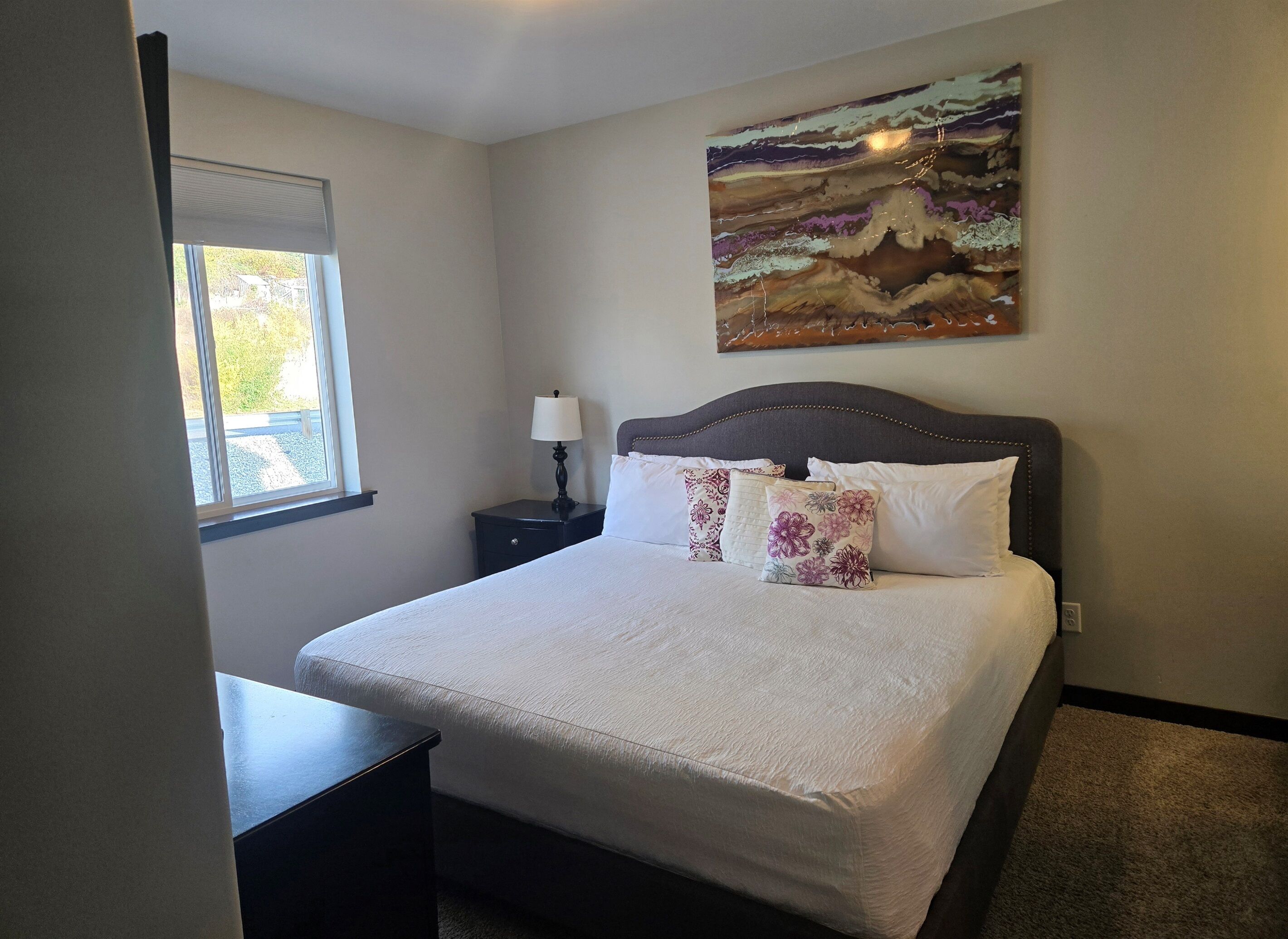 A neatly made bed with floral pillows, a bedside lamp, and a painting on the wall.