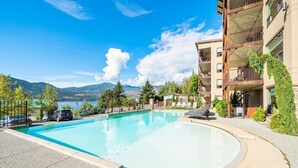 A swimming pool with a view of mountains and a lake, surrounded by a multi-story building with balconies. - Epic Views of Lake Chelan, Modern Condo, Pool, Spa (Manson)