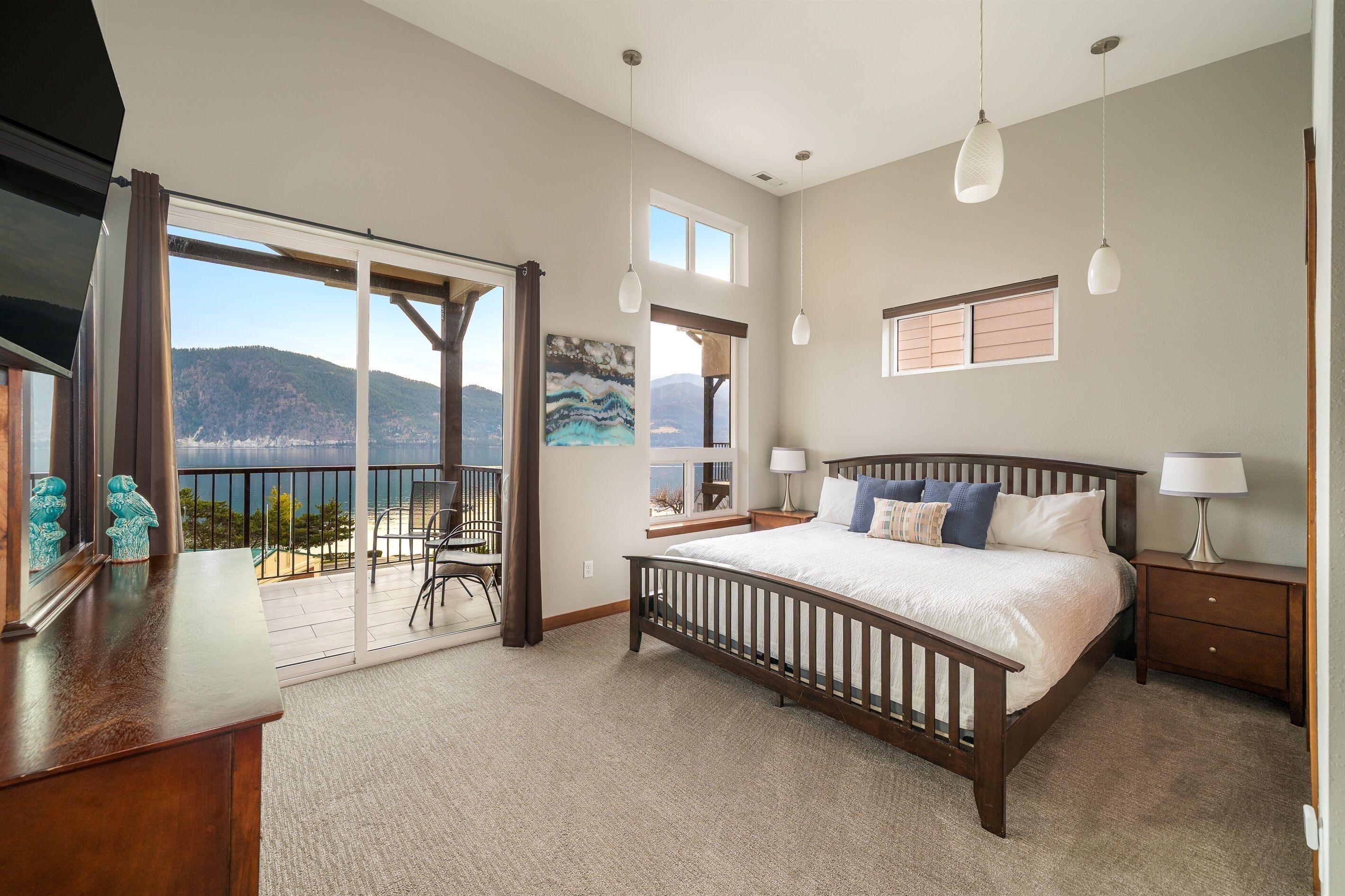 Ein Schlafzimmer mit einem großen Bett, einem Nachttisch, einer Kommode und Blick auf einen Balkon mit einer schönen Landschaft.