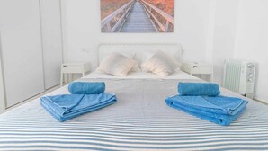 A bedroom with a bed, pillows, a striped blanket, and a painting of a sunset over a beach. - Suncastle Lovely Attic! (Alicante/Alacant)