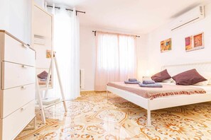 A bedroom with a bed, a wardrobe, a ladder, a window with curtains, and a patterned floor.
