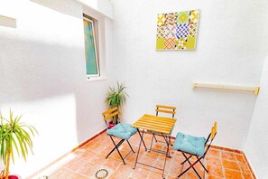 A small patio with a wooden table and two chairs, a potted plant, and a wall-mounted artwork.
