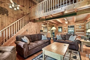 A spacious living room with two brown leather sofas, a wooden coffee table, and a staircase leading to an upper level. - Spacious Cabin with Privacy & Views! Close to All Attractions! (Pigeon Forge)
