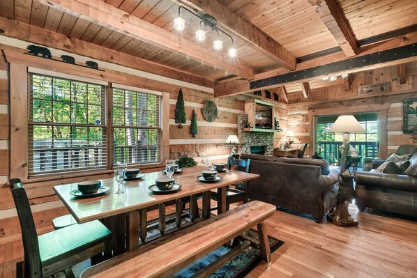 A wooden cabin interior with a dining table, benches, a sofa, and a fireplace. - Spacious Cabin with Privacy & Views! Close to All Attractions! (Pigeon Forge)