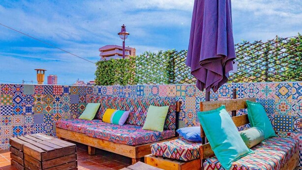 Eine Dachterrasse mit bunten Fliesenwänden, einer Holzbank und einem gemusterten Sofa mit Kissen.