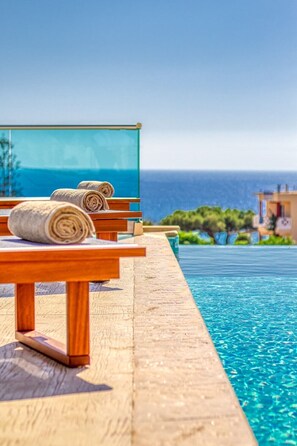 A wooden deck with a pool, a glass balustrade, and towels.