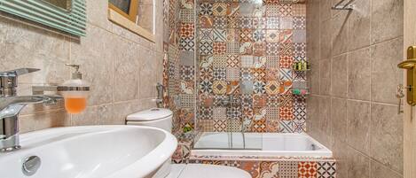 Un baño con lavamanos, inodoro y bañera. Las paredes están cubiertas de azulejos con un diseño decorativo.