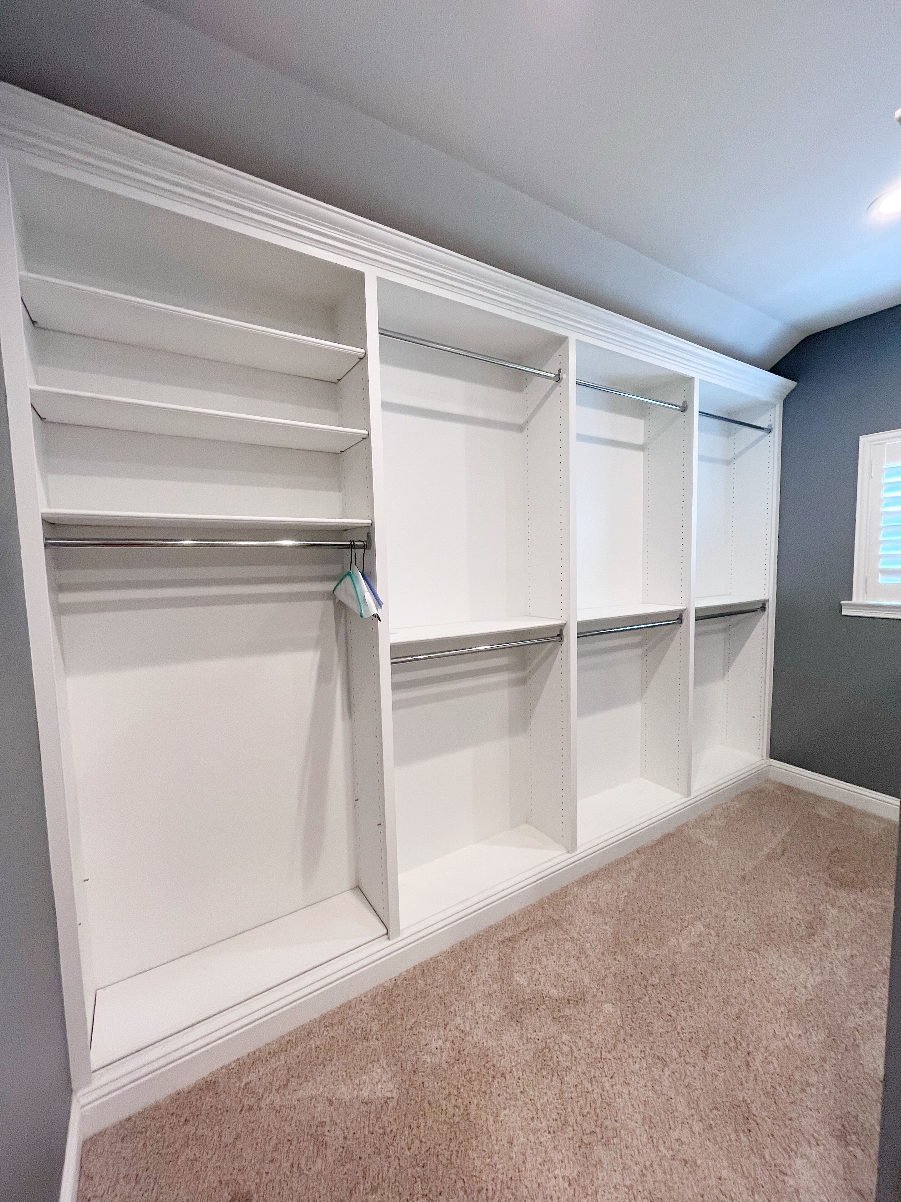 A walk-in closet with multiple shelves and hanging rods, carpeted floor, and a gray wall.