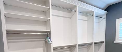A walk-in closet with multiple shelves and hanging rods, carpeted floor, and a gray wall.