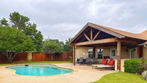 A backyard with a swimming pool, a covered patio with chairs, and a wooden fence. - Fortunata Casa Del Sole Private House and Poolside Escape (Aubrey)