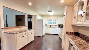 A spacious kitchen with white cabinetry, a granite countertop, and a dark wooden floor. - Fortunata Casa Del Sole Private House and Poolside Escape (Aubrey)