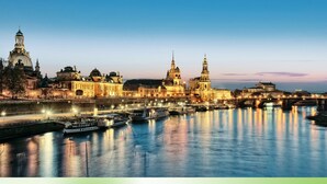 A riverfront cityscape with historic buildings and a bridge at dusk. - "If you want to enjoy life, move to Striesen." (Dresden)