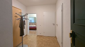 Um corredor com um suporte para casacos, uma porta que dá para um quarto e um chão de madeira.