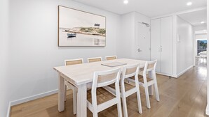 Un coin repas avec une table et des chaises en bois, un tableau encadré au mur et une porte blanche.