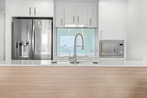 A modern kitchen with stainless steel appliances, a large window, and a wooden countertop.