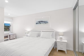 Ein Schlafzimmer mit einem großen Bett, Nachttischen, einem Fenster und einem gerahmten Bild an der Wand.