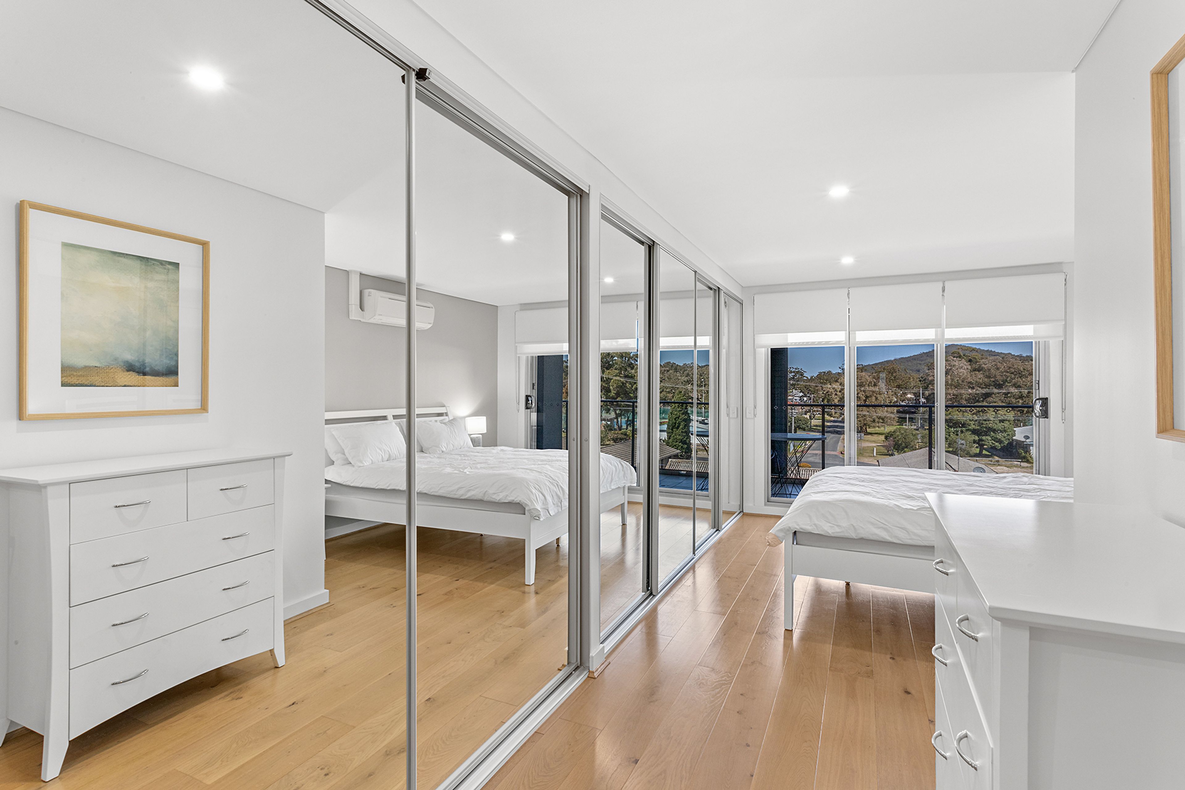 Una camera da letto moderna con un'ampia porta-finestra scorrevole che dà su un balcone, un letto, un comodino e una cassettiera.