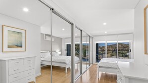 Une chambre moderne dotée d’une grande porte-fenêtre coulissante donnant sur un balcon, d’un lit, d’une table de chevet et d’une commode.