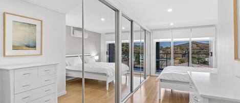 Una camera da letto moderna con un'ampia porta-finestra scorrevole che dà su un balcone, un letto, un comodino e una cassettiera.