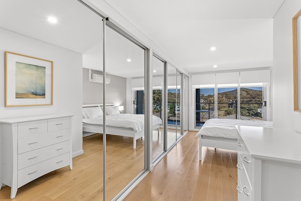 Ein modernes Schlafzimmer mit einer großen Schiebeglas-Tür, die auf einen Balkon führt, einem Bett, einem Nachttisch und einer Kommode.