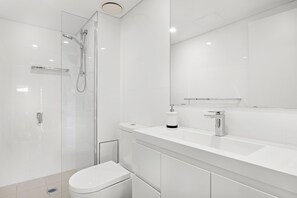 Een moderne badkamer met een douchecabine van glas, een wit toilet en een grote spiegel boven een witte wastafel.