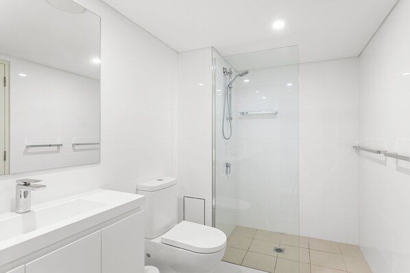 A modern bathroom with a glass-enclosed shower, a white sink, and a toilet.