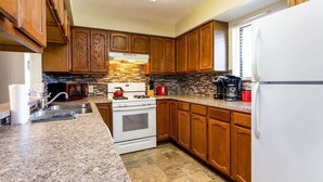 Una cocina con armarios de madera, encimera de granito, estufa y refrigerador.