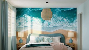 Une chambre avec une grande fresque murale sur le thème de l’océan, un lit avec de nombreux oreillers, deux tables de chevet avec des lampes et un luminaire suspendu.