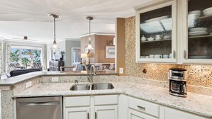 Una cocina con encimera de granito, pileta de acero inoxidable, armarios blancos y cafetera.