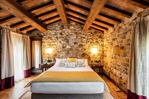 A bedroom with a stone wall, wooden beams, a bed with pillows, and two bedside lamps.