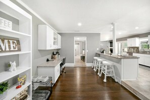 A modern kitchen with white cabinetry, a central island with bar stools, and a visible doorway leading to another room. - Lakeland Highlands Oasis - 3BR Heated Pool Home (Lakeland)