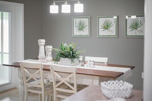 A dining area with a wooden table, white chairs, and a potted plant centerpiece. - Lakeland Highlands Oasis - 3BR Heated Pool Home (Lakeland)