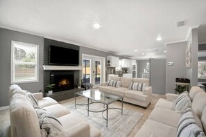 A modern living room with a fireplace, a sofa set, and a glass coffee table. - Lakeland Highlands Oasis - 3BR Heated Pool Home (Lakeland)