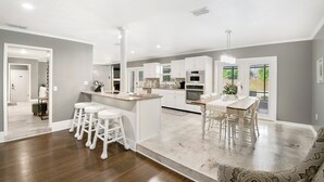 A spacious kitchen with white cabinetry, a central island with stools, and a dining area with a wooden table and chairs.