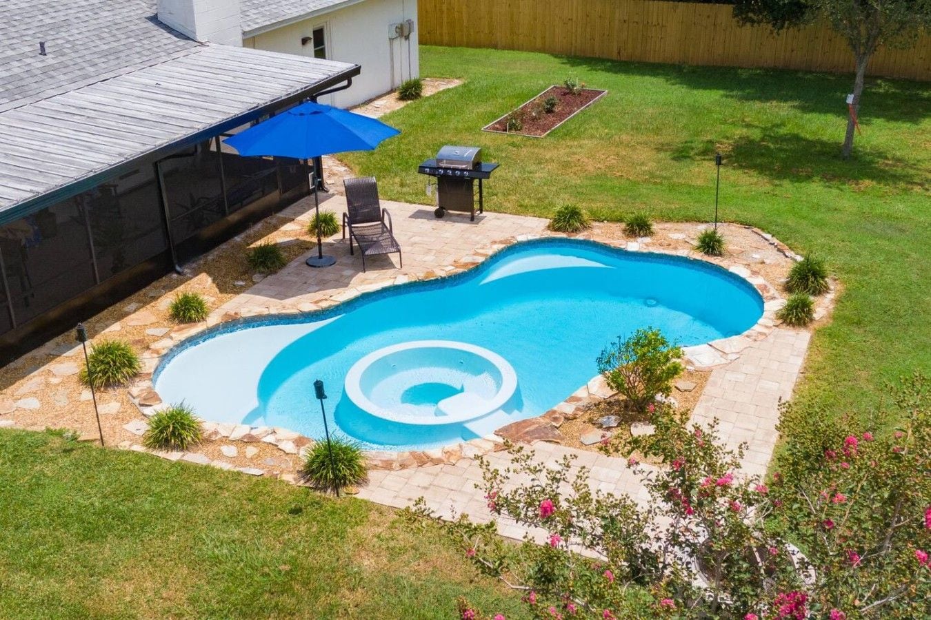 A backyard with a swimming pool, patio furniture, and a barbecue grill.