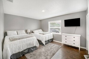 A bedroom with two beds, a dresser, a television, and a window with blinds.