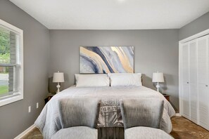 A bedroom with a large bed, two bedside tables with lamps, a window with blinds, and a closet. - Lakeland Highlands Oasis - 3BR Heated Pool Home (Lakeland)