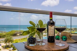 Een fles La Palma wijn, twee wijnglazen, een glas blauwe bessen en een plant op een balkon met uitzicht op zee.