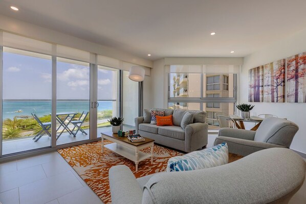 Een moderne woonkamer met een grote schuifpui die uitkomt op een balkon met uitzicht op de oceaan.