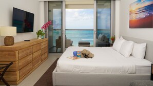 A bedroom with a large bed, a wooden dresser, a TV, and a view of the ocean through a sliding door. - Almost Heaven, Studio Ocean View on the 7th floor (Eagle Beach)