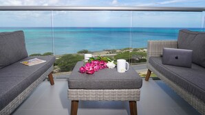 A balcony with two grey sofas, a wicker table, a laptop, a white mug, and a magazine. - Almost Heaven, Studio Ocean View on the 7th floor (Eagle Beach)
