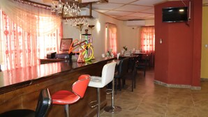 Angolo bar con un bancone, sgabelli da bar rossi e bianchi e un televisore montato a parete.