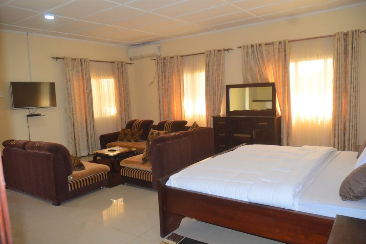 A hotel room with a large bed, a sofa set, a television, and a dresser.