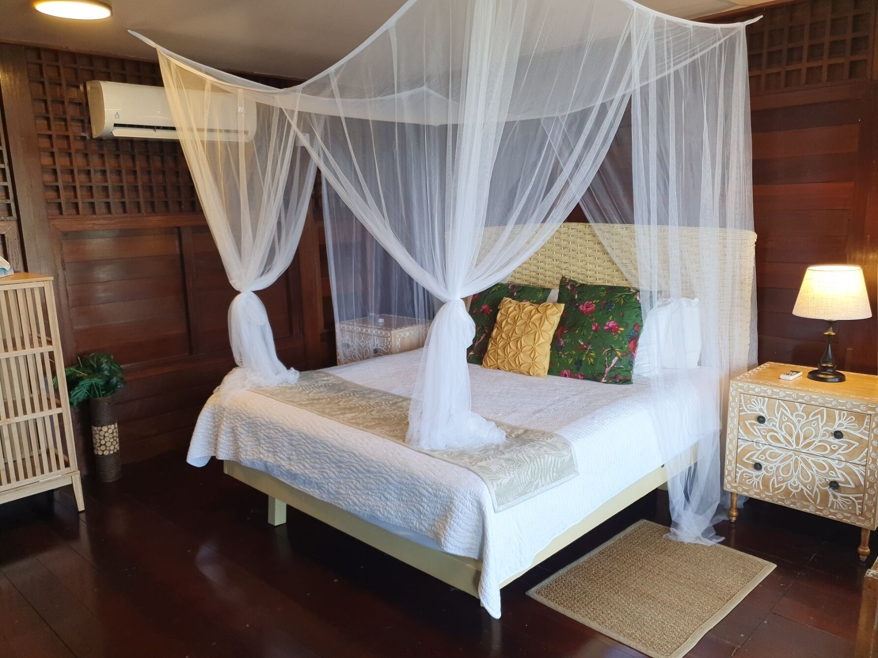 A neatly arranged bedroom with a four-poster bed, a bedside table with a lamp, and a small potted plant.