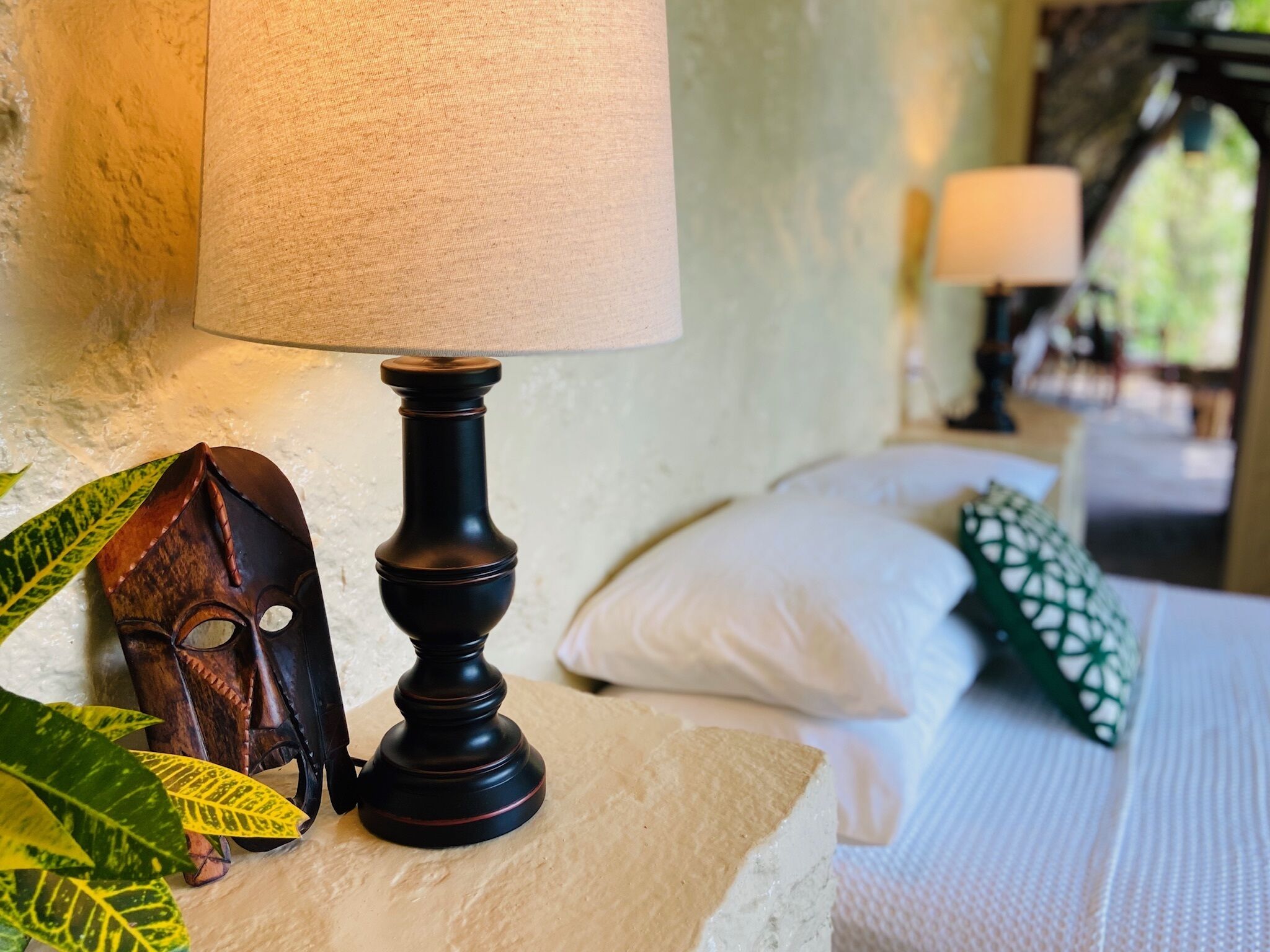 A bed with white bedding, a wooden nightstand with a lamp, and decorative pillows.