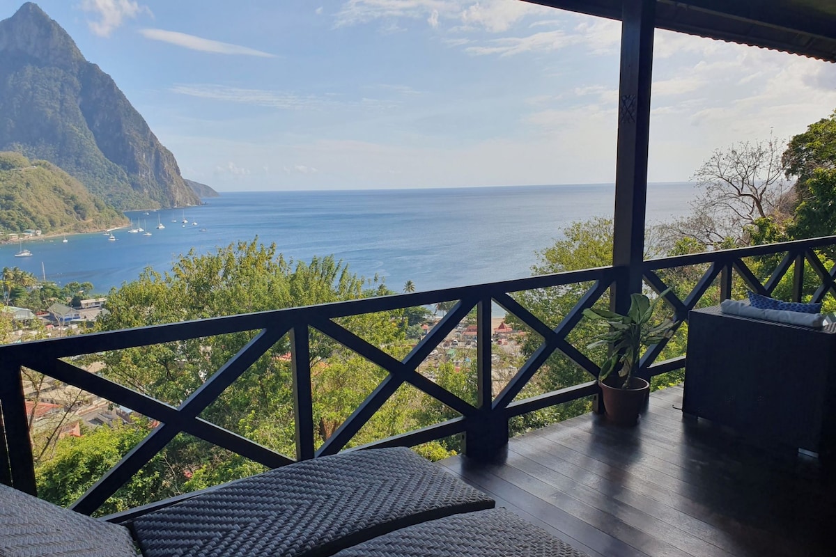 A balcony with wicker furniture overlooking a coastal view with boats and a mountain.